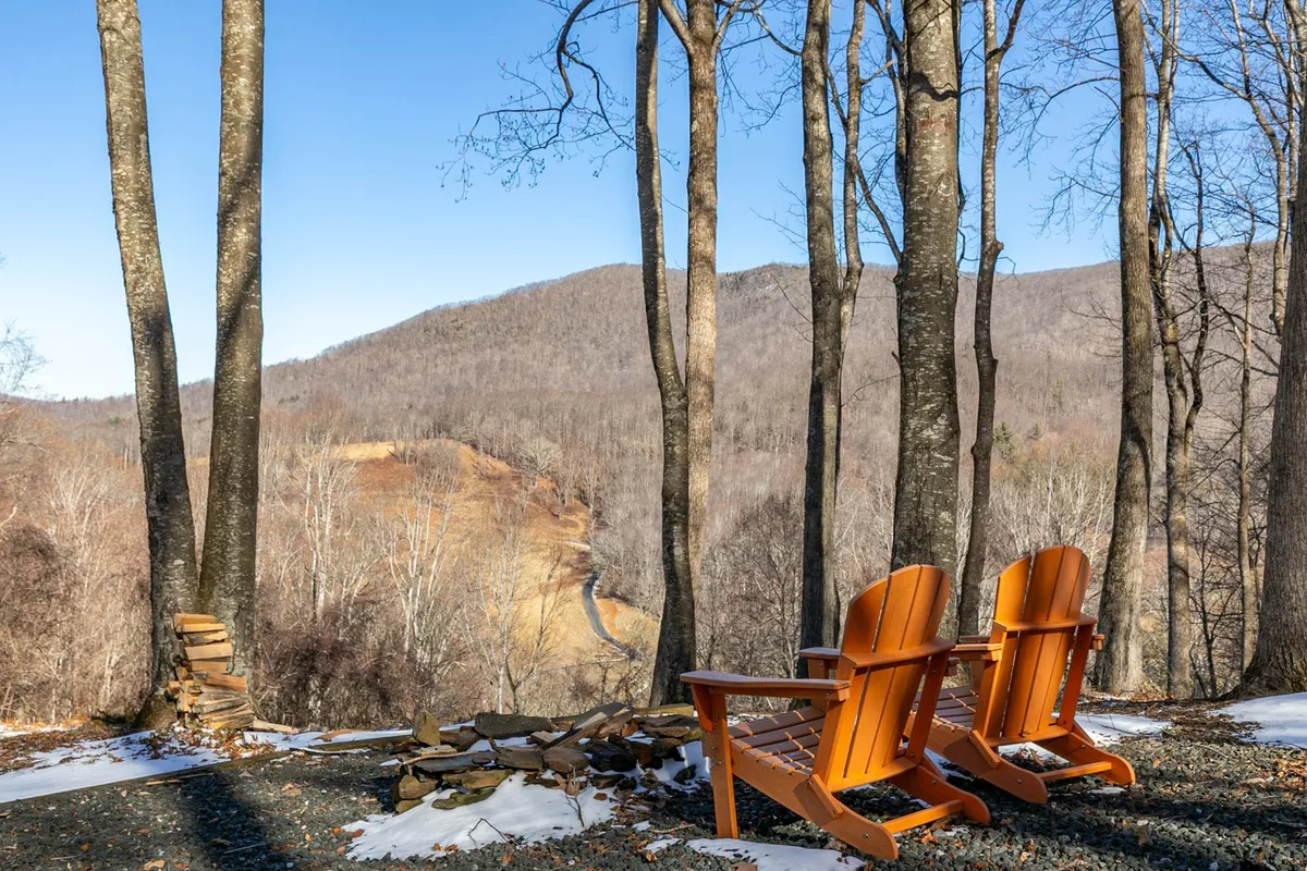 The image shows two wooden chairs facing distant mountains and bare trees, offering an unobstructed panoramic view. The setup invites peaceful moments of contemplation, nature breaks, and perhaps an inspiring spot for remote work or relaxation after a productive day.
