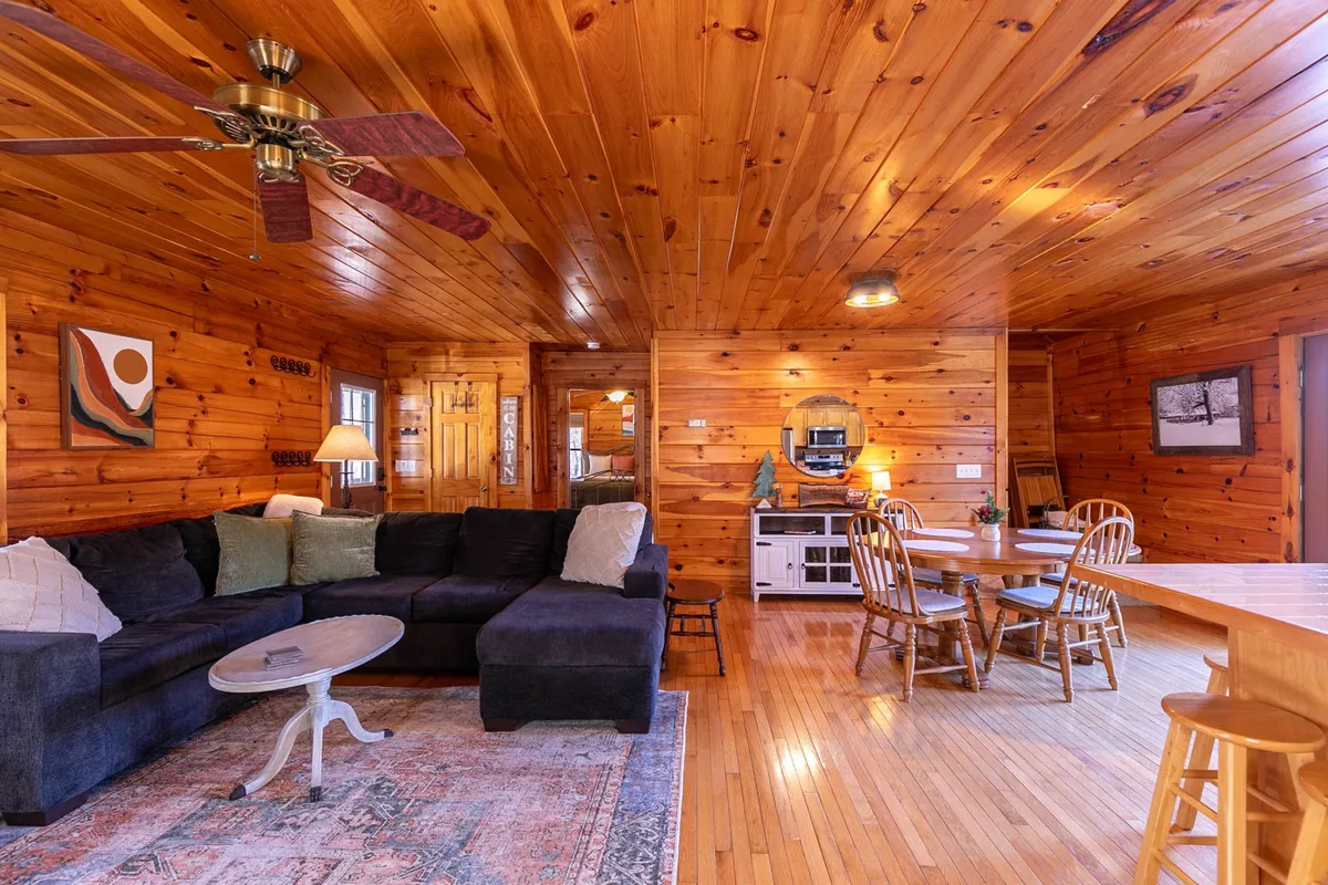 A spacious, open-plan living area with a large sectional sofa, central coffee table, and easy sightlines to a dining area. Warm wood ceilings and tasteful artwork create a homey, inviting environment perfect for group gatherings and family game nights.