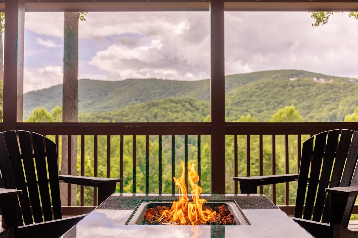 This scene captures Adirondack chairs arranged around a fire pit on a wooden deck, overlooking a panoramic mountain view. The wooden railing frames an expansive vista, inviting guests to relax, socialize, and immerse themselves in the surrounding nature.