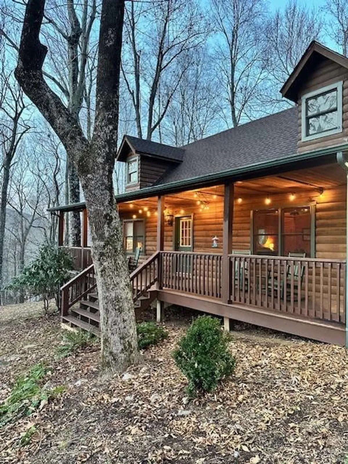 A cozy log cabin sits nestled among tall trees, featuring a spacious wooden porch and inviting outdoor seating area. The tranquil setting highlights the seamless connection between the cabin and the surrounding natural landscape, offering a sense of retreat and adventure.