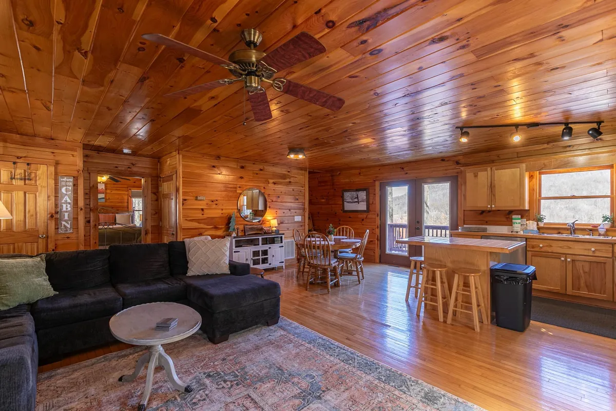 A broad view of the interior showcasing a wooden ceiling, a comfortable sectional sofa, a kitchen area, and a dining table. The harmonious layout encourages group activities, from cooking to relaxing and sharing meals.
