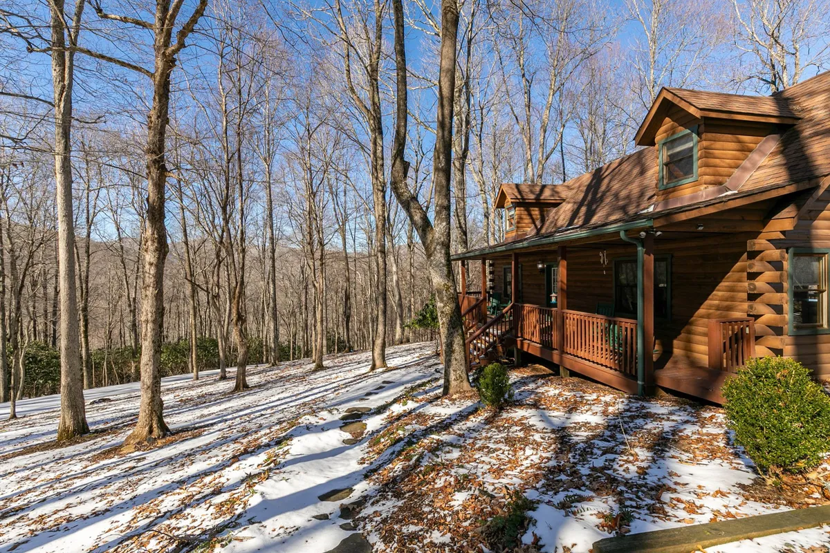 An exterior winter scene featuring the wooden cabin, snow-covered ground, and deck with railing. The trees and serene landscape evoke a sense of seclusion and seasonal transformation, emphasizing the property’s winter wonderland aspect.
