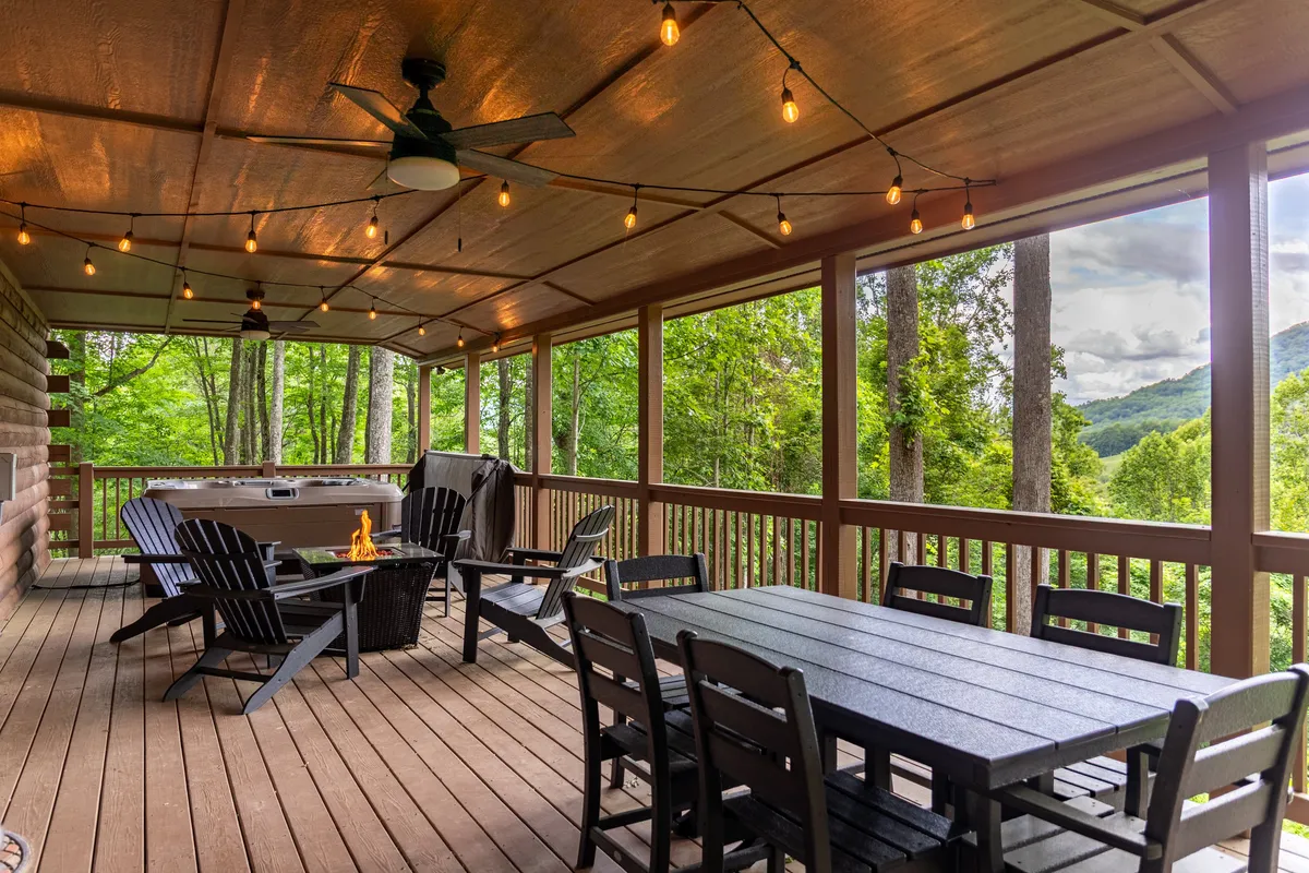 This image captures an inviting outdoor scene featuring a dining table, fire pit, and bubbling hot tub, all set beneath hanging lights. The surrounding natural greenery and wood accents evoke a sense of connection with nature and relaxation. Multiple gathering areas are visible, including the fire pit and hot tub, which are central to the section's content.